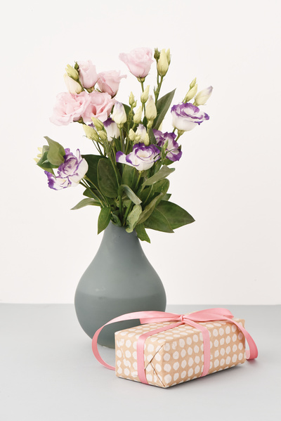Gift with Bow is in Front of Vase of Flowers on Grey Background
